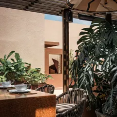 The bar area is surrounded by lush greenery, making it feel integrated with the garden. Woven bar stools and a wooden countertop add to the natural, earthy material palette of this outdoor bar design.
