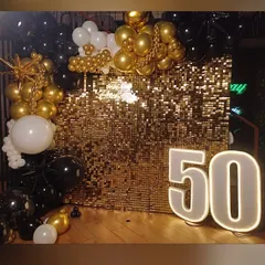 We created a glamorous 50th birthday with this stunning gold shimmer wall. The backdrop is framed by an organic balloon arrangement in black, gold, and white, with a "Happy Birthday" neon sign and large "50" marquee numbers adding to the sparkle.