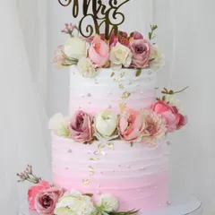 This two-tiered pink ombre cake is the picture of romance, perfect for a wedding or anniversary. It's adorned with a cascade of lifelike sugar flowers in shades of pink and white, with a custom "Mr & Mrs" topper.