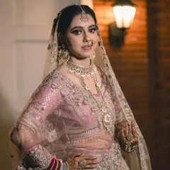 A confident and classic bridal portrait. The bride looks directly at the camera, showcasing her full wedding day attire, including the beautiful jewelry and henna.