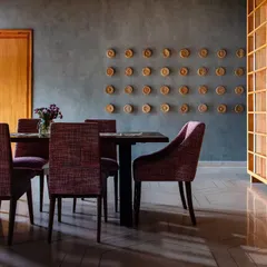 The dining lounge at Anthea Pharma, where earthy-toned fabrics add a pop of color against the raw, textured backdrop. Delicately carved circular artwork contrasts beautifully with the rustic concrete wall.