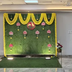 A baby shower photo booth with a lush green grass wall, marigold garlands, and hanging lotus props.