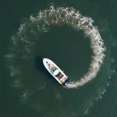 A stunning top-down aerial view of a white yacht creating a perfect circle with its wake in the dark green ocean. This creative drone shot turns a pre-wedding moment into a piece of art.