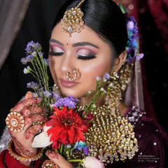 A close-up of a contemporary bridal hairstyle, showing a neat bun adorned with purple and white flowers, complementing the soft, romantic makeup.