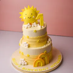 A burst of sunshine for a first birthday celebration. This cheerful two-tier cake features a bright yellow and white design with fondant suns, clouds, and rainbows, perfect for celebrating your little one's big day.
