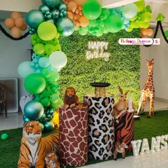 We used a lush green wall as the backdrop for this jungle-themed first birthday. The decor includes an organic balloon arch, animal-print plinths for the cake, large animal props, and illuminated letters for the birthday boy's name.