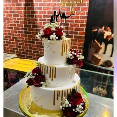 A classic three-tier wedding cake with a modern twist. This design features a gold drip effect, accented with fresh red roses and baby's breath, and topped with a "Just Married" silhouette topper.