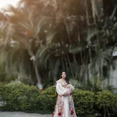 A wide shot showing the beautiful scale of the outdoor location. The mom-to-be stands peacefully in her floral gown, framed by tall palm trees and soft, natural light.