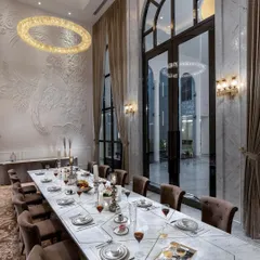 The formal dining room in The Grand Alabaster is designed for grand entertaining. A long marble table sits beneath a dramatic ring chandelier, with double-height arched windows providing a view of the courtyard and filling the space with an air of majesty.