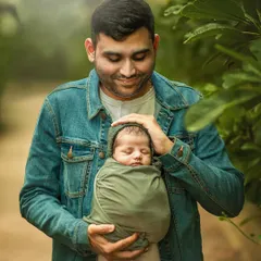 A father gently holds his swaddled newborn, looking down with a soft, loving expression. This close-up portrait beautifully captures the quiet, powerful bond between a father and his new baby.