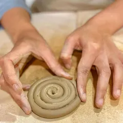 The coiling technique involves rolling out long ropes of clay and building them up, layer by layer. Here, a student is starting the base for a coiled pot.
