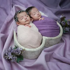 An angled view of the sleeping twins, showcasing the full setup with the heart basket, soft purple fabric, and delicate floral accents.