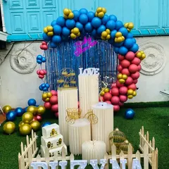 A full view of the outdoor baby shower decoration, showing the combination of blue, red, and gold balloons with a full set of props on an artificial grass lawn.