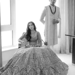 A classic black and white portrait of the couple, the bride seated while the groom stands, creating a formal and elegant composition.