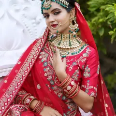 A full view of a North Indian bride in a stunning red lehenga, adorned with green and white Kundan jewellery.
