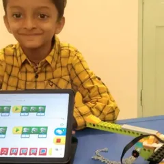A student proudly poses with his helicopter project, demonstrating the code he wrote on the tablet to make the propellers spin.