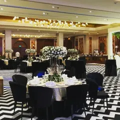A closer look at the table setting for a formal corporate dinner. Tall, elegant centerpieces with white flowers, classic black chairs, and a striking chevron floor come together to create a polished and high end dining experience for guests.