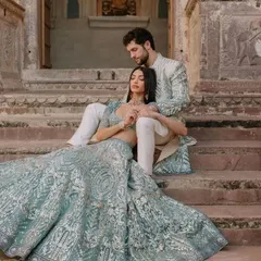 A breathtaking, regal portrait. The couple is dressed in coordinated powder blue outfits with intricate silver embroidery, showcasing a luxurious and ethereal look for a grand wedding.