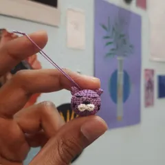 A close-up of a tiny purple cat phone charm. The micro-crochet technique allows for a lot of detail in a very small space.