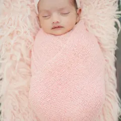 A detailed close-up of a swaddled newborn girl. The soft knit wrap and matching headband add a touch of sweetness while keeping the focus on the baby's serene expression.