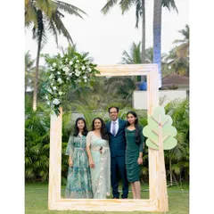 A family poses inside a large, rustic wooden photo frame we set up for an outdoor event. The frame is adorned with a corner floral piece, perfectly complementing the natural surroundings.