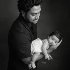 A powerful black and white portrait of a father holding his newborn. The dramatic lighting creates a beautiful, artistic image.