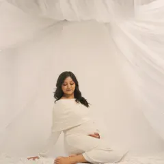Serenity in white. This full-length portrait shows the mother-to-be seated amidst a sea of soft, white fabric, creating a dreamy and peaceful atmosphere. It's a timeless image of calm and grace.
