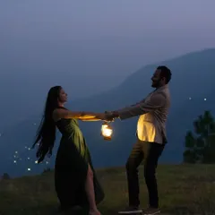 A playful and romantic moment captured during a night shoot in the mountains. The couple dances, holding a lantern whose light catches the movement of her dress, with the distant city lights adding to the magical atmosphere.