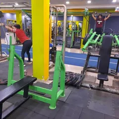 Members working on different goals in the same space. One person is doing a cable exercise for their back while another uses a plate-loaded machine for pull-ups, showing the variety of equipment available.