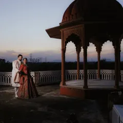A wide shot capturing the couple against the historic architecture of Umaid Palace at dusk. This image sets a moody and romantic scene, emphasizing the grandeur of the location and the intimacy of the moment.