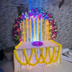 A beautiful setup for a Pooja or small ceremony at home. The table is decorated with a floral arch and strings of marigolds, creating a sacred and festive space.