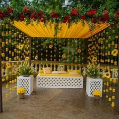 This beautiful outdoor mehendi seating area is covered with a canopy of yellow fabric and hanging marigold strings. The white lattice bench and side tables create a comfortable and picturesque spot for the bride.
