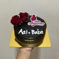 A bold and striking black anniversary cake for "Aai Baba," decorated with fresh red roses.