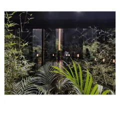 Looking out from the Black Pavilion into the garden it frames. The dark, porous mesh walls create a stark contrast with the vibrant green of the plants, heightening the sense of being in a sanctuary.