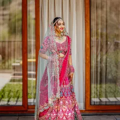 A vision in pink! This stunning full-length portrait showcases the intricate details of the bride's vibrant lehenga. Her happy and confident smile truly lights up the frame.
