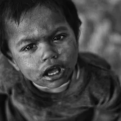 This powerful black and white portrait of a young child looking directly up at the camera is filled with raw emotion. The high-contrast monochrome effect highlights the dirt on his face and the intensity in his eyes, creating a truly unforgettable image.