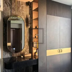 This is another view of the integrated vanity and wardrobe system, showing how different textures like fluted panels, marble-look walls, and dark wood come together. The open shelving next to the mirror provides easy access to everyday items.