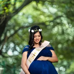 An outdoor maternity portrait in a beautiful park. The mother-to-be is cradling her belly, surrounded by the soft greens of nature.