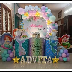 This Little Mermaid theme for Advita's 7th birthday is perfect for an indoor celebration. The setup includes character cutouts, mermaid-tail-patterned pedestals, and a pastel rainbow balloon arch.
