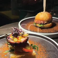 We specialize in gourmet canapés and small plates that delight the senses. This pairing shows our range, featuring a savory open-faced toast with cured meat and microgreens alongside a miniature gourmet slider, perfect for cocktail hours.
