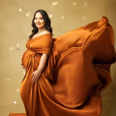 A stunning solo portrait featuring a dramatic flying fabric effect. The mother-to-be looks powerful and radiant as the rust-colored gown flows behind her.