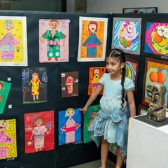 A young artist proudly stands by her collection of work at our annual exhibition. This moment, where a child sees their creations displayed professionally, is a massive confidence booster and a core part of our program.