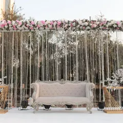 A chic and modern stage for a day wedding, with a backdrop of shimmering silver strings and a lush floral border. The classic white sofa completes the look.