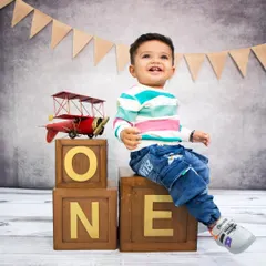 Ready for takeoff! This little boy celebrates turning one with a cheerful smile, sitting beside a vintage toy airplane prop.