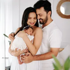 A lovely family photo from a newborn session. The parents are all smiles as they cradle their sleeping baby, dressed in coordinated white outfits for a clean and timeless look.