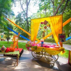 A beautifully decorated food cart at an outdoor event, draped in colorful yellow and blue fabrics. This can be used to serve anything from welcome drinks to desserts.