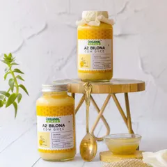 Two jars of A2 Bilona Cow Ghee are styled in a bright, airy setting on a small wooden stool. The clean background and touch of greenery give this shot a fresh, modern, and healthy feel.