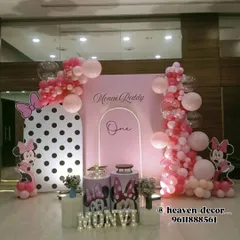 An elegant Minnie Mouse first birthday setup in pink and white. The decor features a modern arched backdrop with neon light accents, Minnie Mouse balloon columns, and custom-printed plinths.