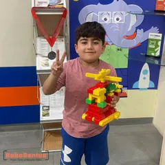A first-grade student proudly holds up the LEGO helicopter he constructed during a Tinkering course session. Students learn to follow instructions and then innovate on their own designs, building confidence and creativity.