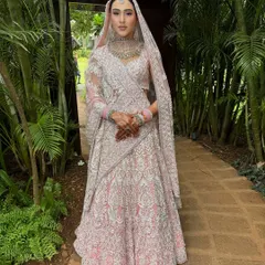 The full bridal look against a lush green backdrop. The intricate white embroidery on her pink lehenga is breathtaking, and the makeup was designed to enhance her natural beauty without distracting from the outfit's details.